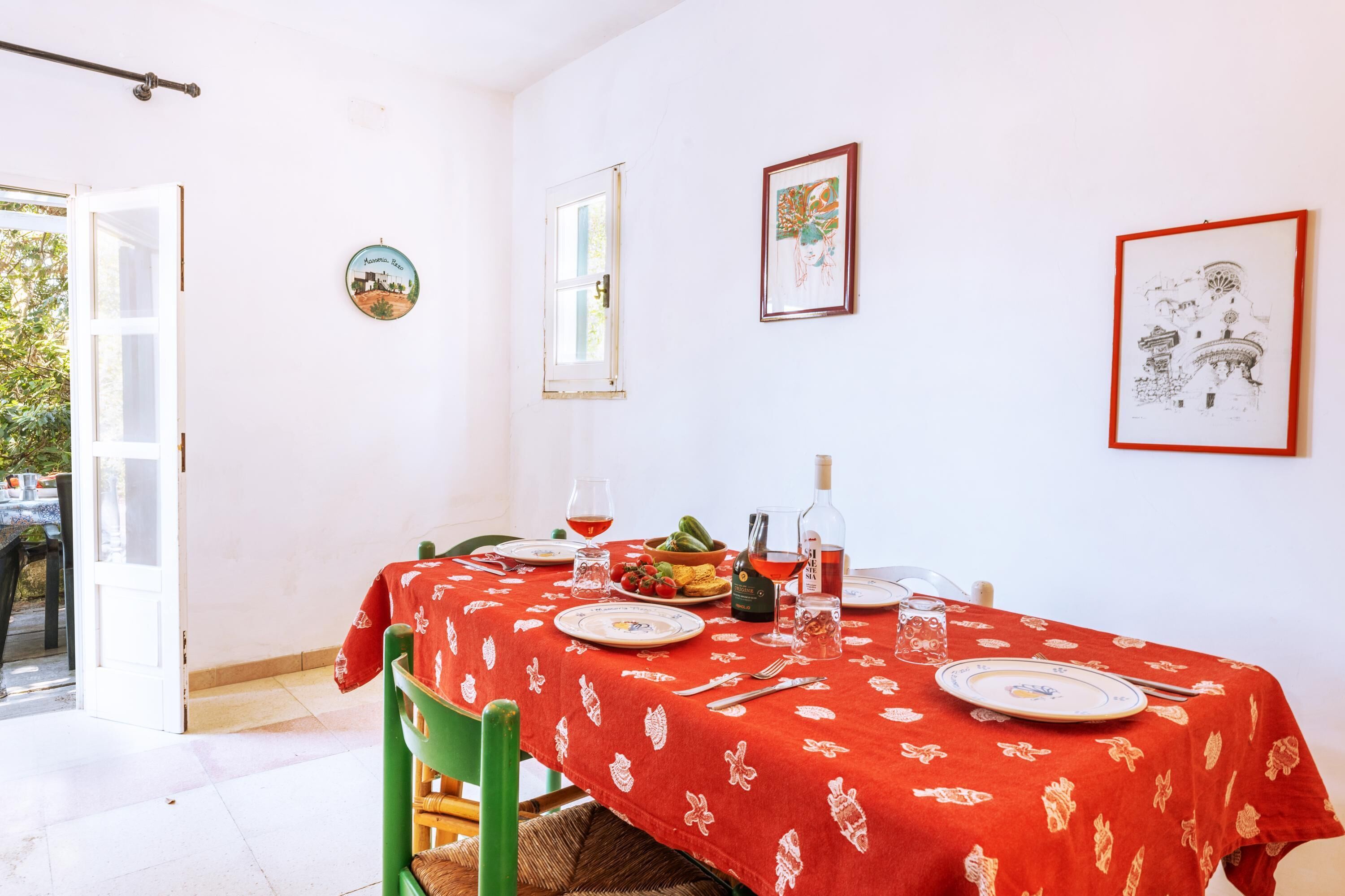 Un coin repas avec une table dressée pour deux personnes, une bouteille de vin et un saladier de fruits.