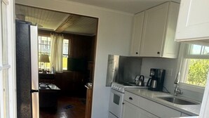 Una cocina compacta con armarios blancos, una estufa de acero inoxidable y una cafetera.