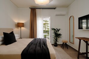 Un dormitorio con cama, lámpara, planta en maceta, un taburete pequeño, espejo y vista al exterior.