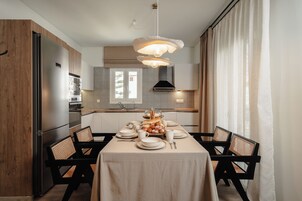 Una cocina moderna con una mesa de comedor dispuesta para cuatro personas, que incluye una exhibición central de frutas, sillas de madera y una lámpara colgante.