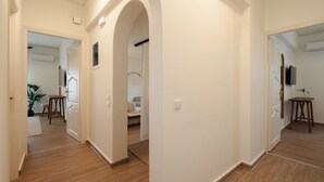 A hallway with wooden flooring, white walls, and an arched doorway leading to a living area with a sofa and a TV. - Naxian Nest suites & houses (Naxos)