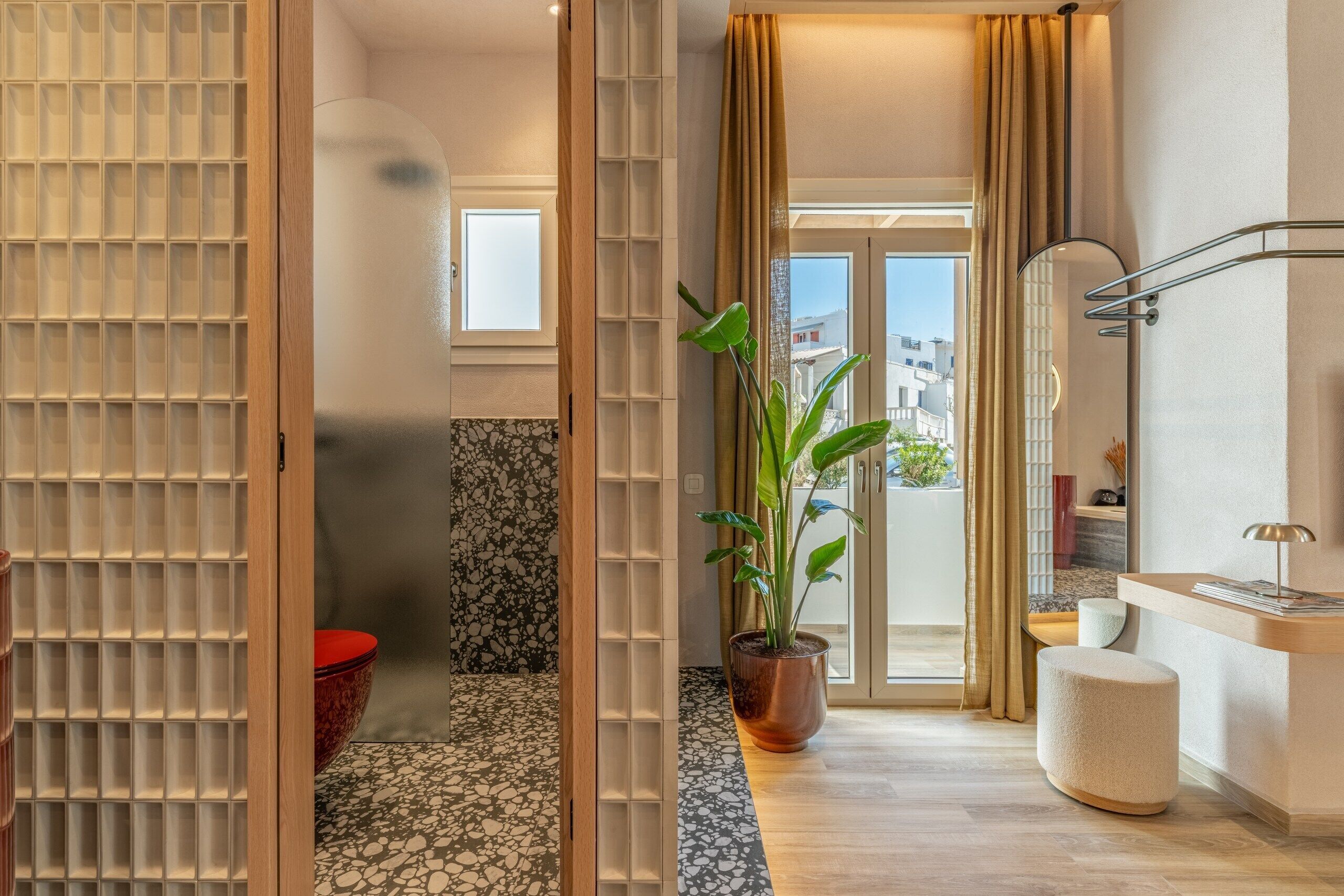 Un baño moderno con un espejo grande, una planta en maceta, un cuenco rojo y vistas al exterior.