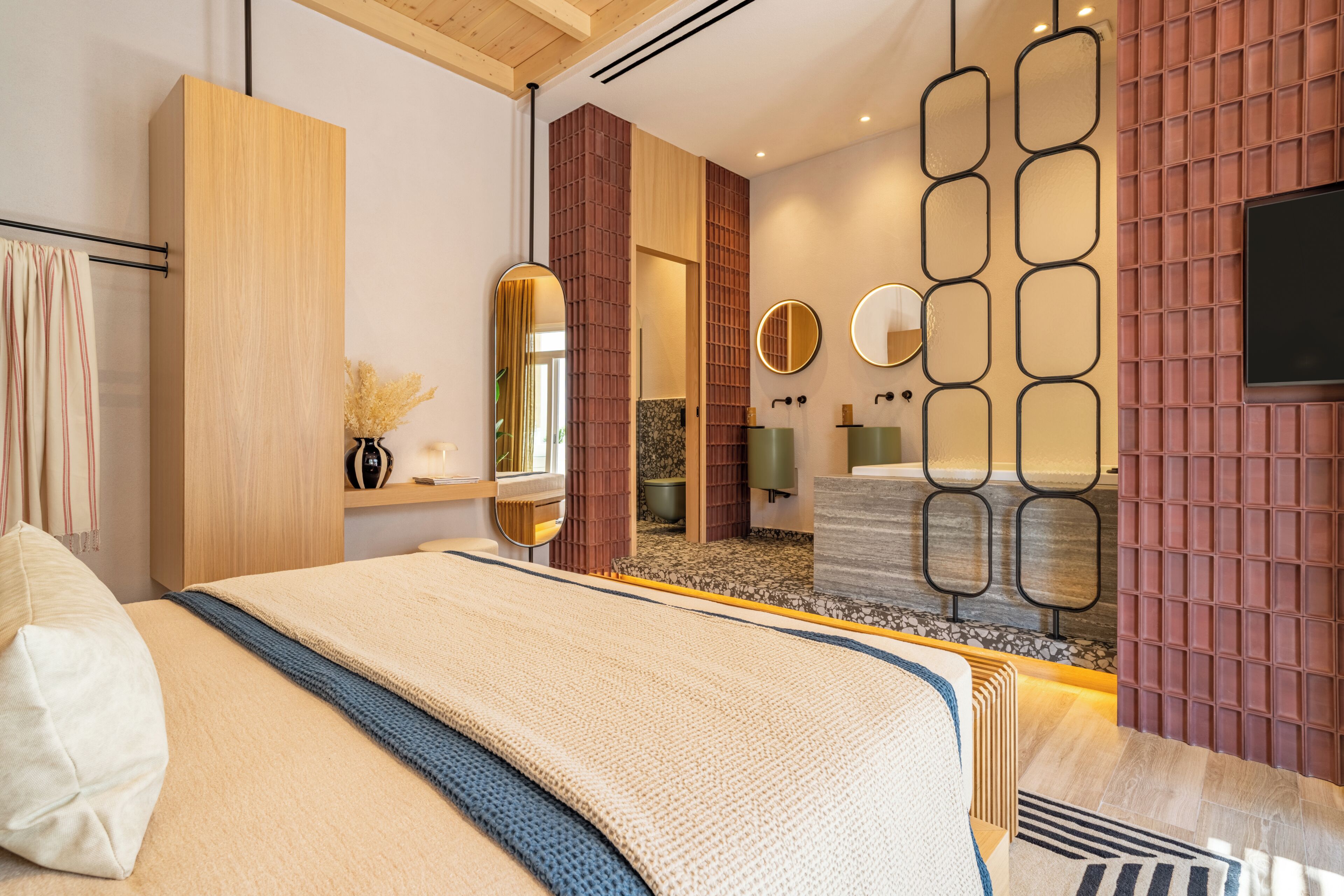 Ein modernes Schlafzimmer mit einem großen Bett, einem Holzschrank, einem Spiegel und einem durchgegangene Tür erkennbaren Badezimmer.