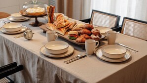 Ein Frühstücksbuffet mit verschiedenen Backwaren und Brot, Tellern, Tassen und Besteck auf einem Tisch.