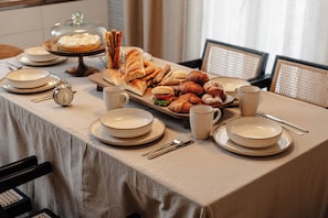 Un buffet de petit-déjeuner avec divers pâtisseries et pains, des assiettes, des tasses et des couverts disposés sur une table.