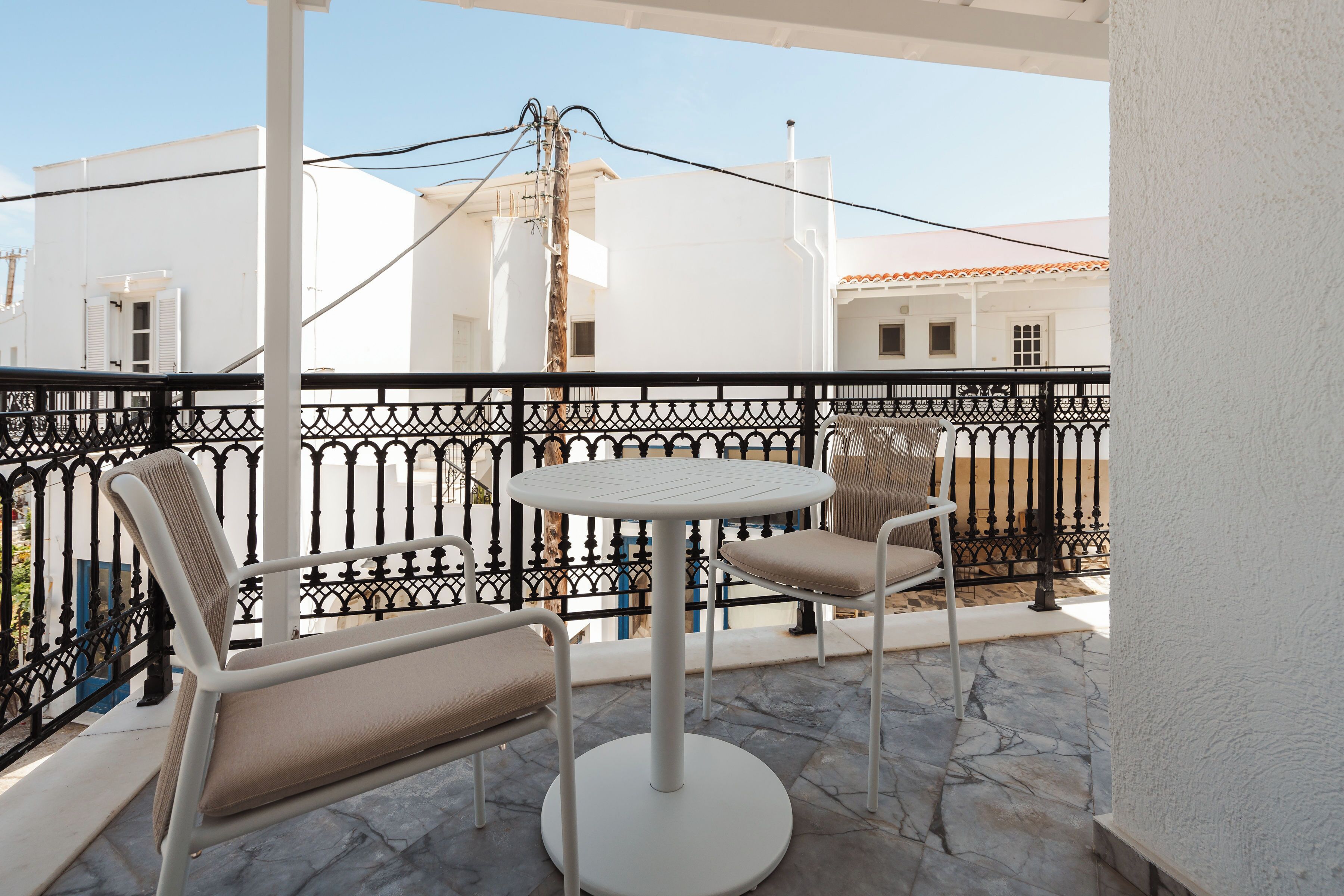 Ein Balkon mit rundem Tisch und zwei Stühlen, weißen Wänden und einem schwarzen Metallgeländer.