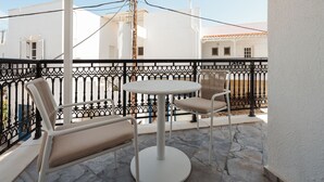 Ein Balkon mit rundem Tisch und zwei Stühlen, weißen Wänden und einem schwarzen Metallgeländer.