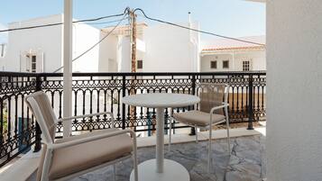 Ein Balkon mit rundem Tisch und zwei Stühlen, weißen Wänden und einem schwarzen Metallgeländer.