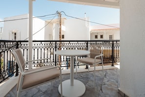 Un balcon avec une table ronde et deux chaises, des murs blancs et une rambarde en métal noir.