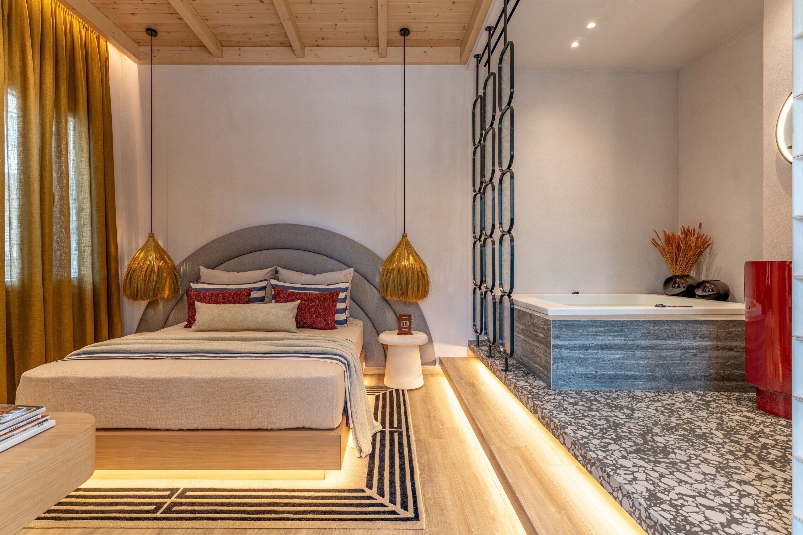 A modern bedroom with a large bed, bedside lamps, a nightstand, and a bathroom with a bathtub and a wall-mounted toilet.