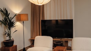 A modern living room with a flat-screen TV, two white armchairs, a coffee table with decorative items, and a large woven light fixture. - Naxian Nest suites & houses (Naxos)