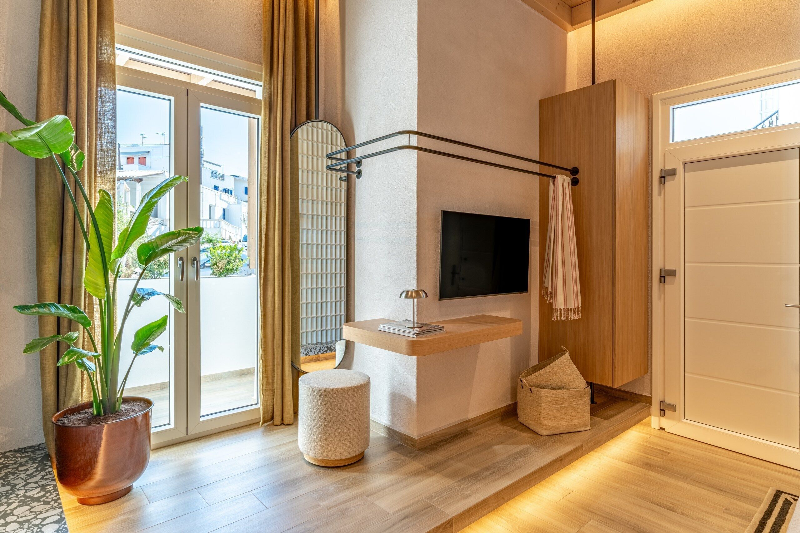 A modern room with a large window, a flat-screen TV, a wooden cabinet, and a potted plant.