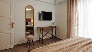 A hotel room with a bed, a TV mounted on the wall, a wooden desk, a mirror, and a door. - Naxian Nest suites & houses (Naxos)