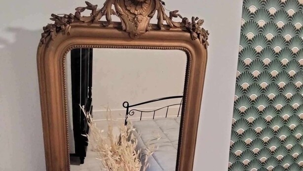 A mirror with a decorative frame, a vase with dried flowers, and a metal lamp on a marble surface. - The Cozy Baroque Nest—Linens Provided (La Bourboule)