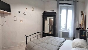 A bedroom with a bed, a mirror, a wardrobe, and a television on a stand. - The Cozy Baroque Nest—Linens Provided (La Bourboule)