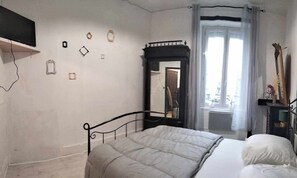 A bedroom with a bed, a mirror, a wardrobe, and a television on a stand. - The Cozy Baroque Nest—Linens Provided (La Bourboule)