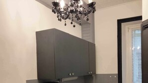 A compact kitchen with a microwave, toaster, and kettle on the counter, a dark cabinet above, and a window with a view. - The Cozy Baroque Nest—Linens Provided (La Bourboule)