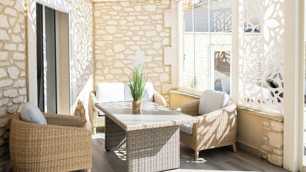 A sunlit patio with wicker furniture, a stone wall, and a decorative screen. - Family domaine with pool in the Camargue region (Arles)