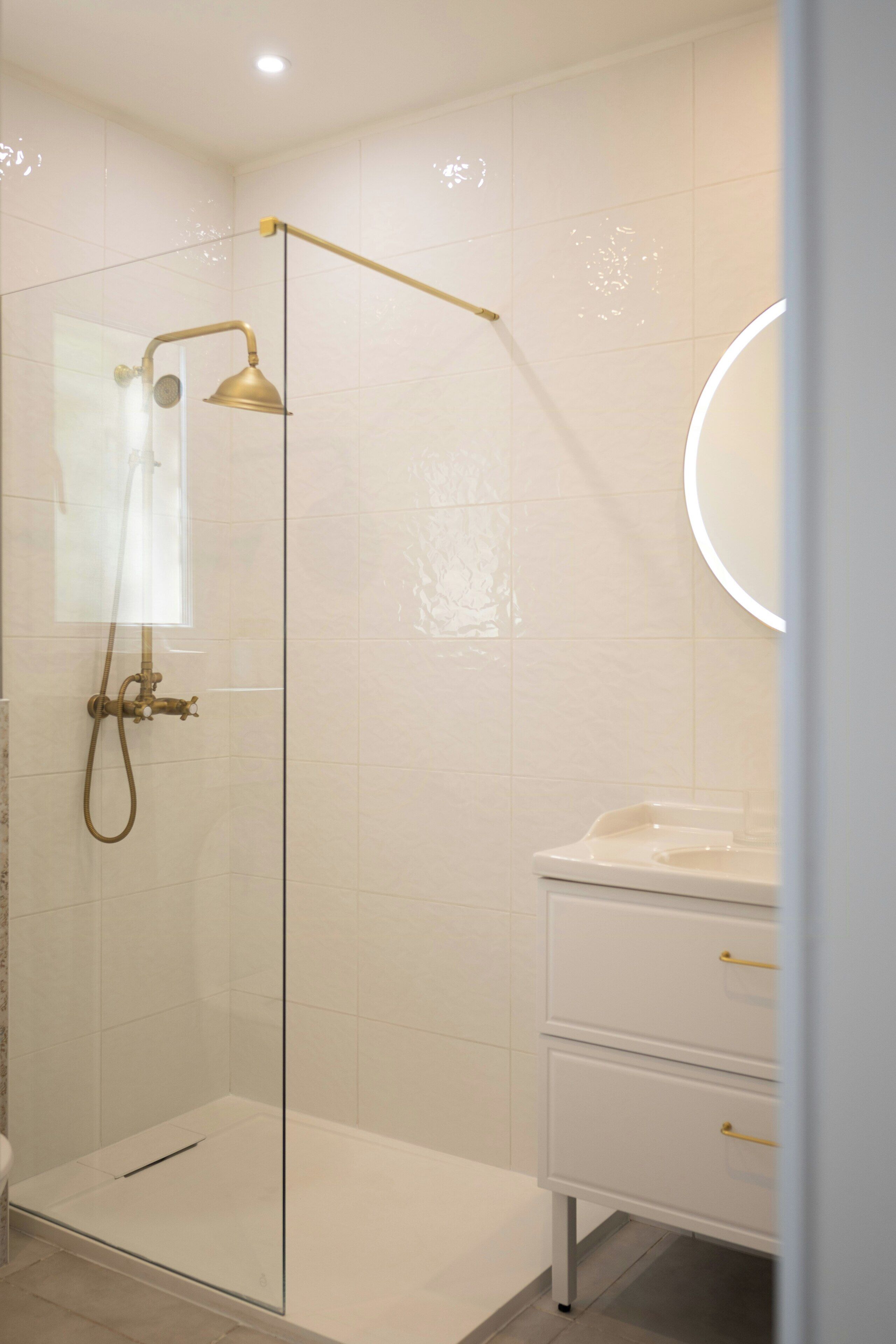A modern bathroom with a glass-enclosed shower, a white sink with a mirror, and a white vanity with drawers.