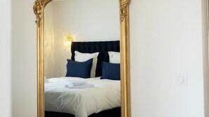 A room with a large ornate mirror, a bed with dark headboard and pillows, and a wall-mounted light fixture. - Family domaine with pool in the Camargue region (Arles)