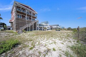 A beachfront property with a multi-story building, a staircase leading to the entrance, and a sandy beach area. - Paradis Marin | Oceanfront + Private Pool (Oak Island)