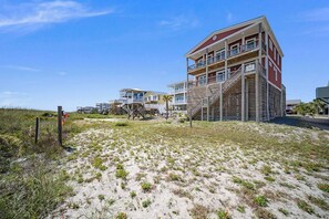 A beachfront hotel with multiple levels, outdoor staircases, and a sandy beach area. - Paradis Marin | Oceanfront + Private Pool (Oak Island)