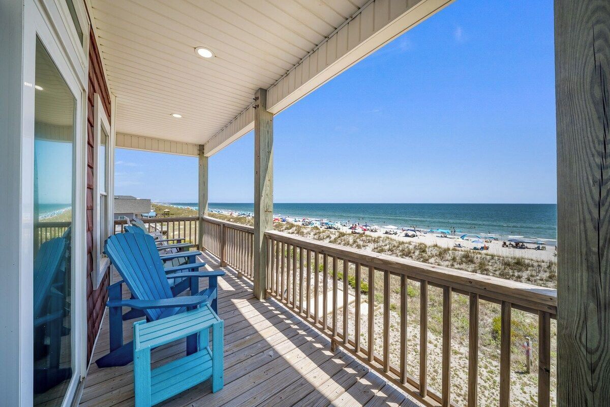 Eine Holzterrasse mit Stühlen mit Blick auf einen Strand.