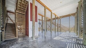 Ett rymligt interiört utrymme med högt i tak och synliga träbjälkar, ett betonggolv och utsikt genom stora fönster.