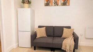 Ein Wohnzimmer mit grauem Sofa, einem beigen Teppich und einem weißen Kühlschrank.