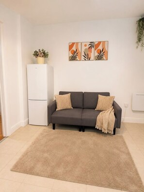 Ein Wohnzimmer mit grauem Sofa, einem beigen Teppich und einem weißen Kühlschrank.