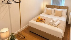 Ein Schlafzimmer mit Bett, Nachttisch, Lampe und einem Fenster mit Vorhängen.
