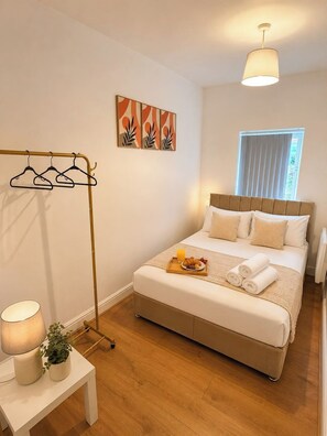 Ein Schlafzimmer mit Bett, Nachttisch, Lampe und einem Fenster mit Vorhängen.