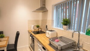 Eine kleine Küche mit Waschmaschine, Toaster, Spüle und einem Fenster mit Jalousien.