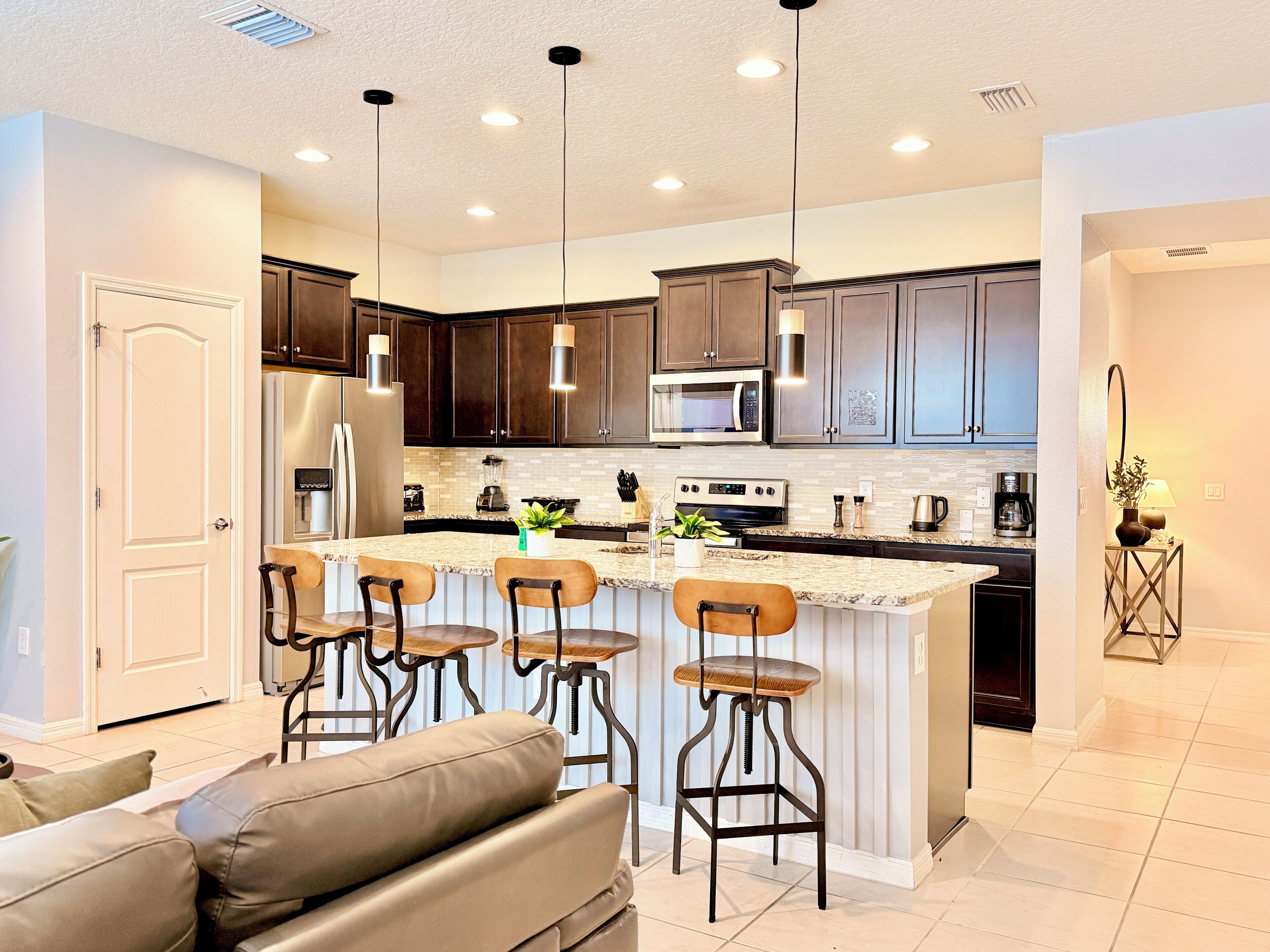 A modern kitchen with dark cabinets, a central island with bar stools, a refrigerator, a microwave, and a stove.