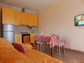 A small, cozy room with a bed, a kitchen area with yellow cabinets, a dining table with chairs, and a television mounted on the wall. - Residence La Cicala Palmi (Palmi)
