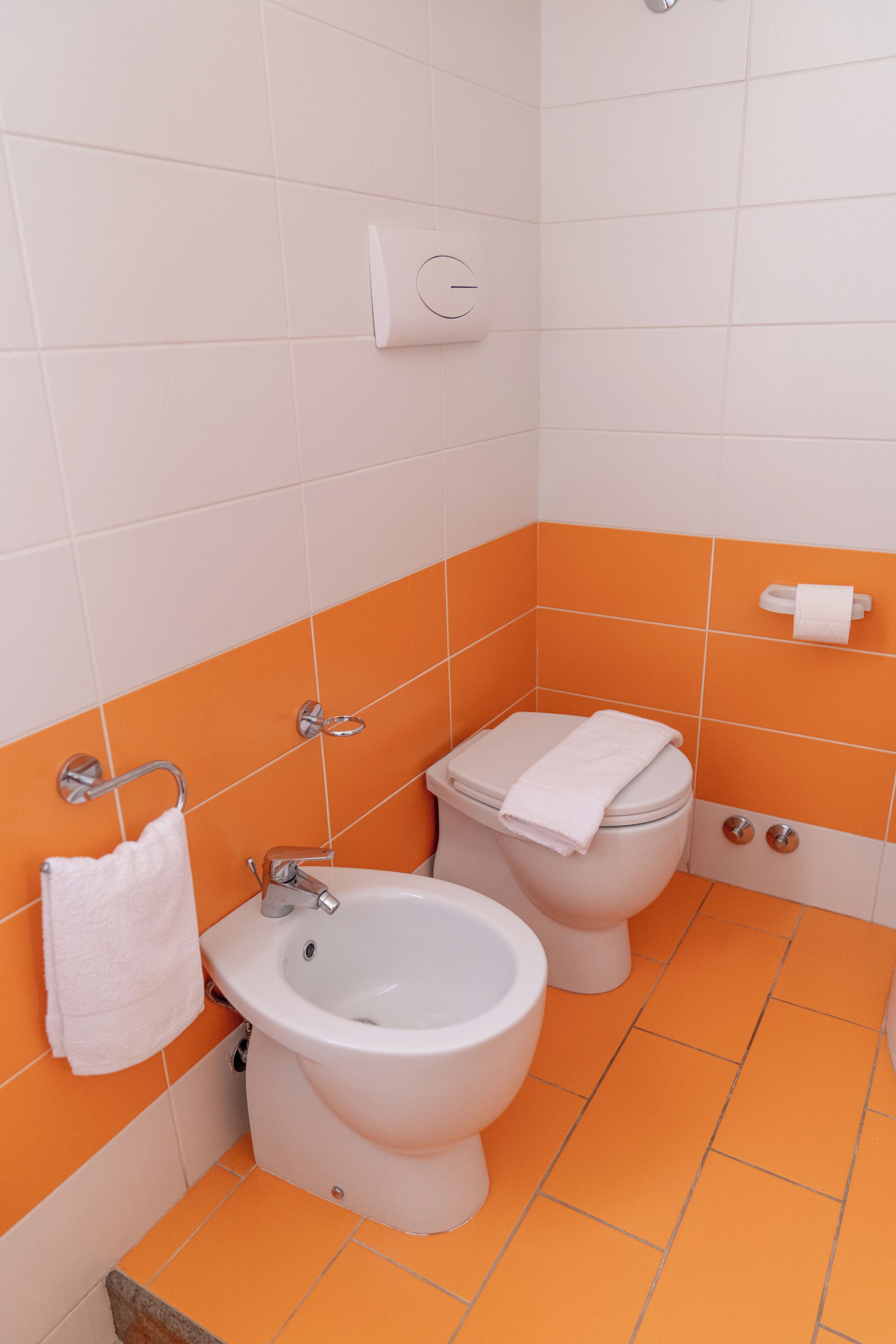 A bathroom with a bidet, toilet, and sink, featuring orange and white tiles.
