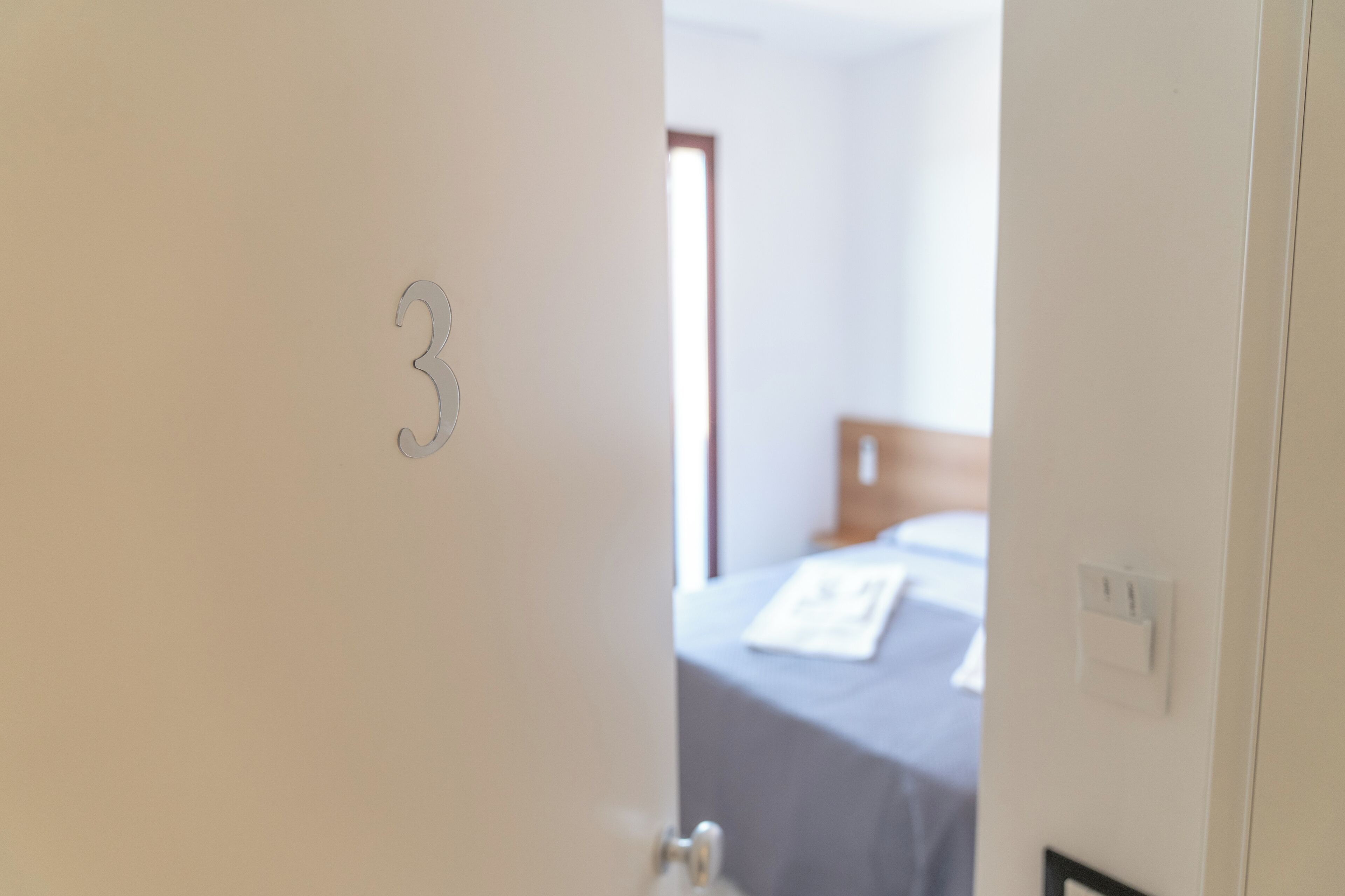 Une porte portant le numéro 3, qui donne sur une pièce comprenant un lit et une fenêtre.