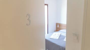 Une porte portant le numéro 3, qui donne sur une pièce comprenant un lit et une fenêtre.