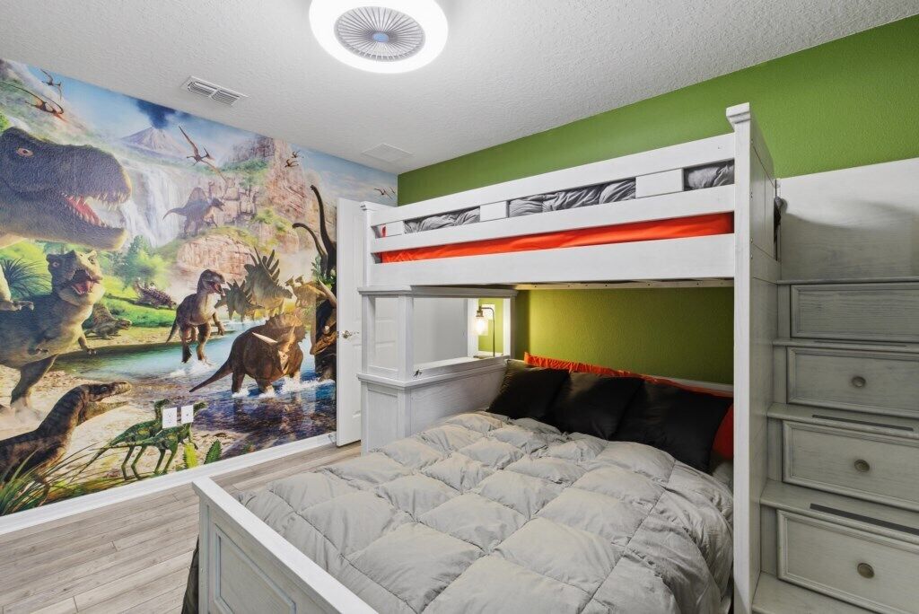 Une chambre avec des lits superposés et une fresque représentant des dinosaures sur le mur.