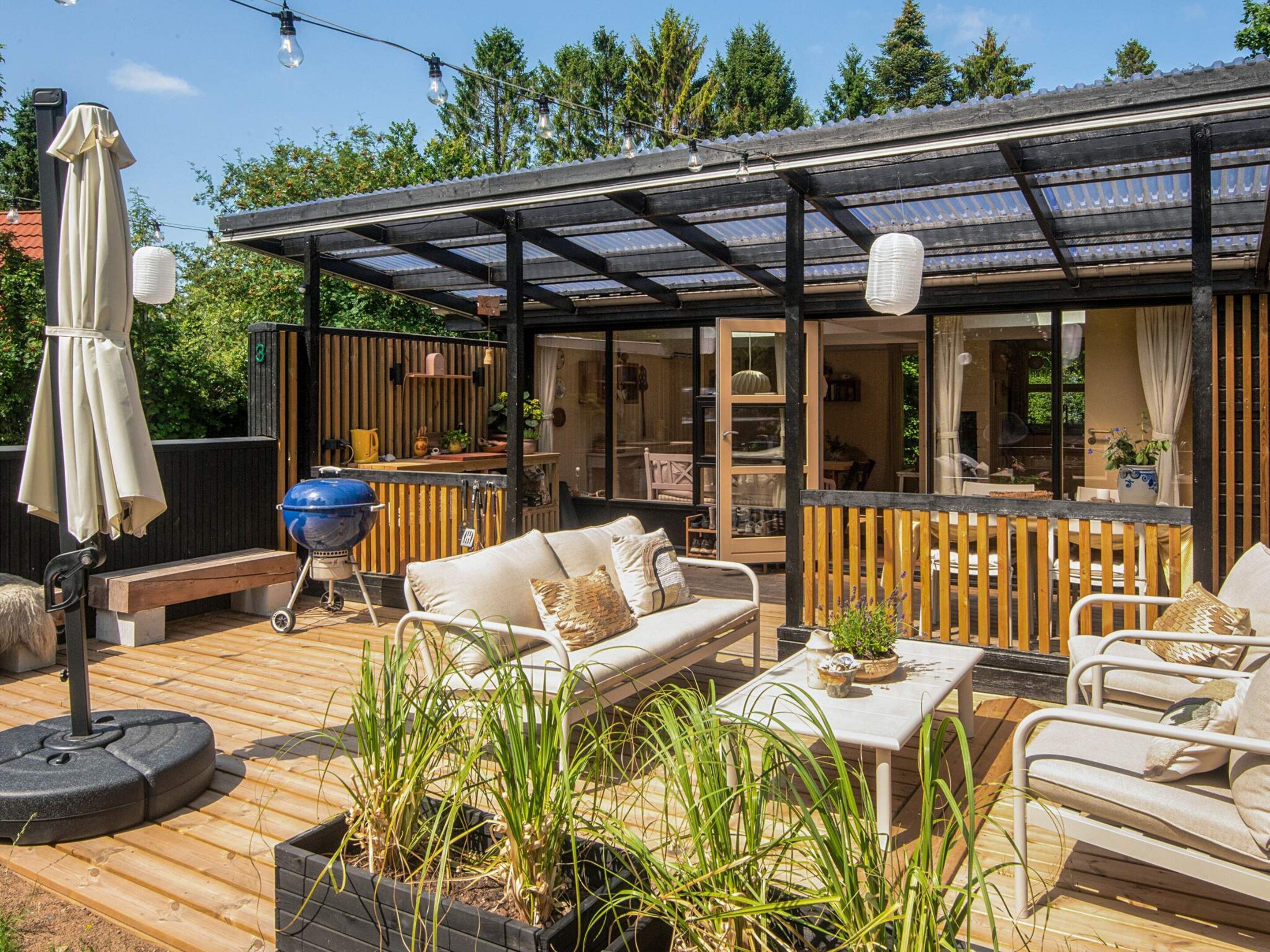 An outdoor deck with a covered seating area, a barbecue grill, and potted plants.