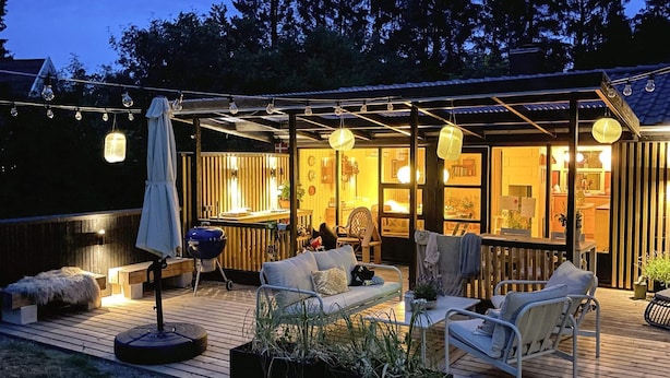 An outdoor patio area with a wooden deck, seating, and string lights. - 4 Star Holiday Home in Ebeltoft (Ebeltoft)