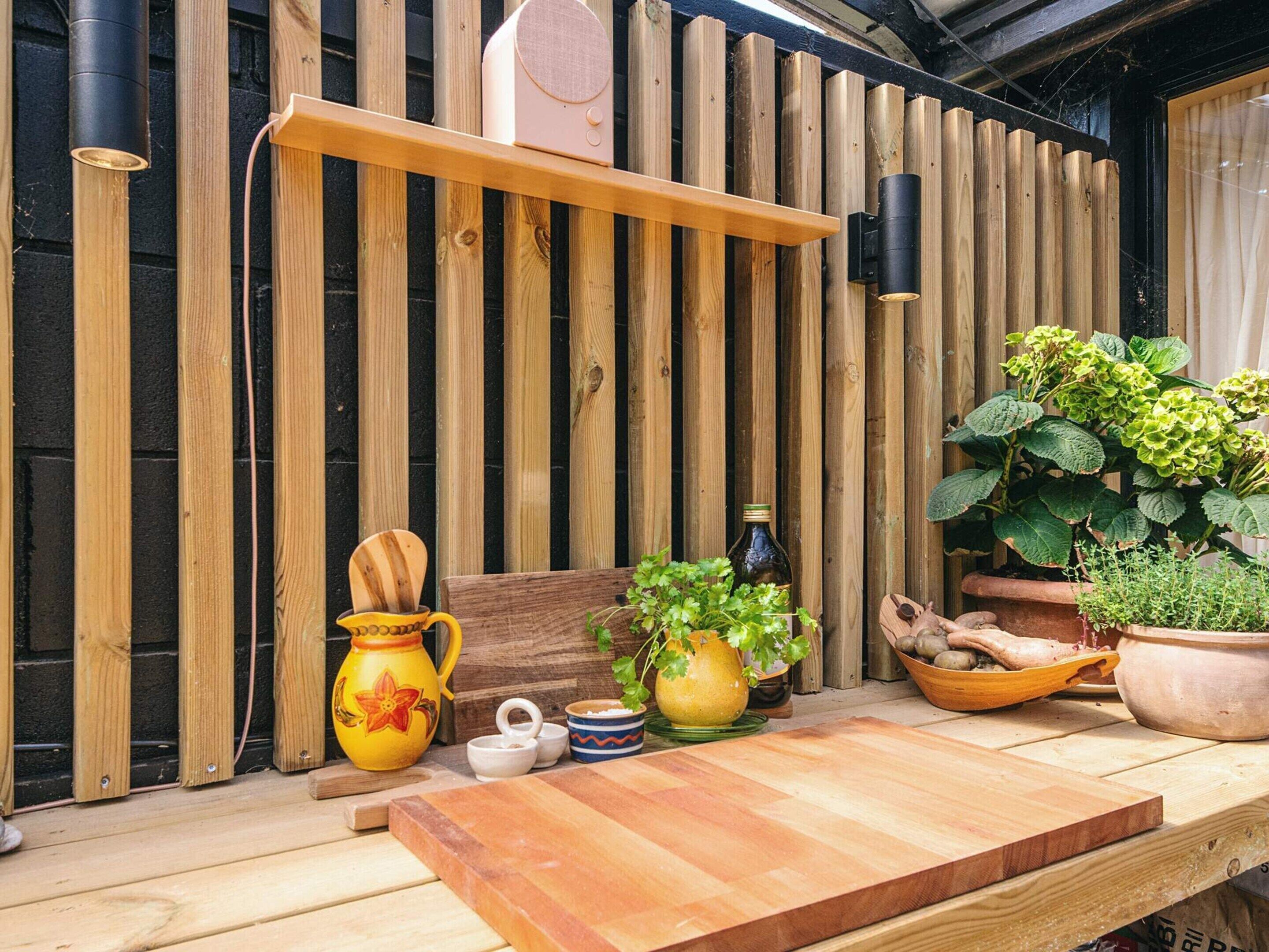 A wooden table with a cutting board, a yellow pitcher, a wooden bowl, and a potted plant.