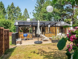 Un patio moderno al aire libre con una barbacoa, zona de estar y un espacio cubierto con vistas al bosque circundante.