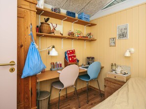 Ein gemütliches Zimmer mit einem Holztisch, zwei Stühlen, einem Bett und Regalen mit verschiedenen Gegenständen.