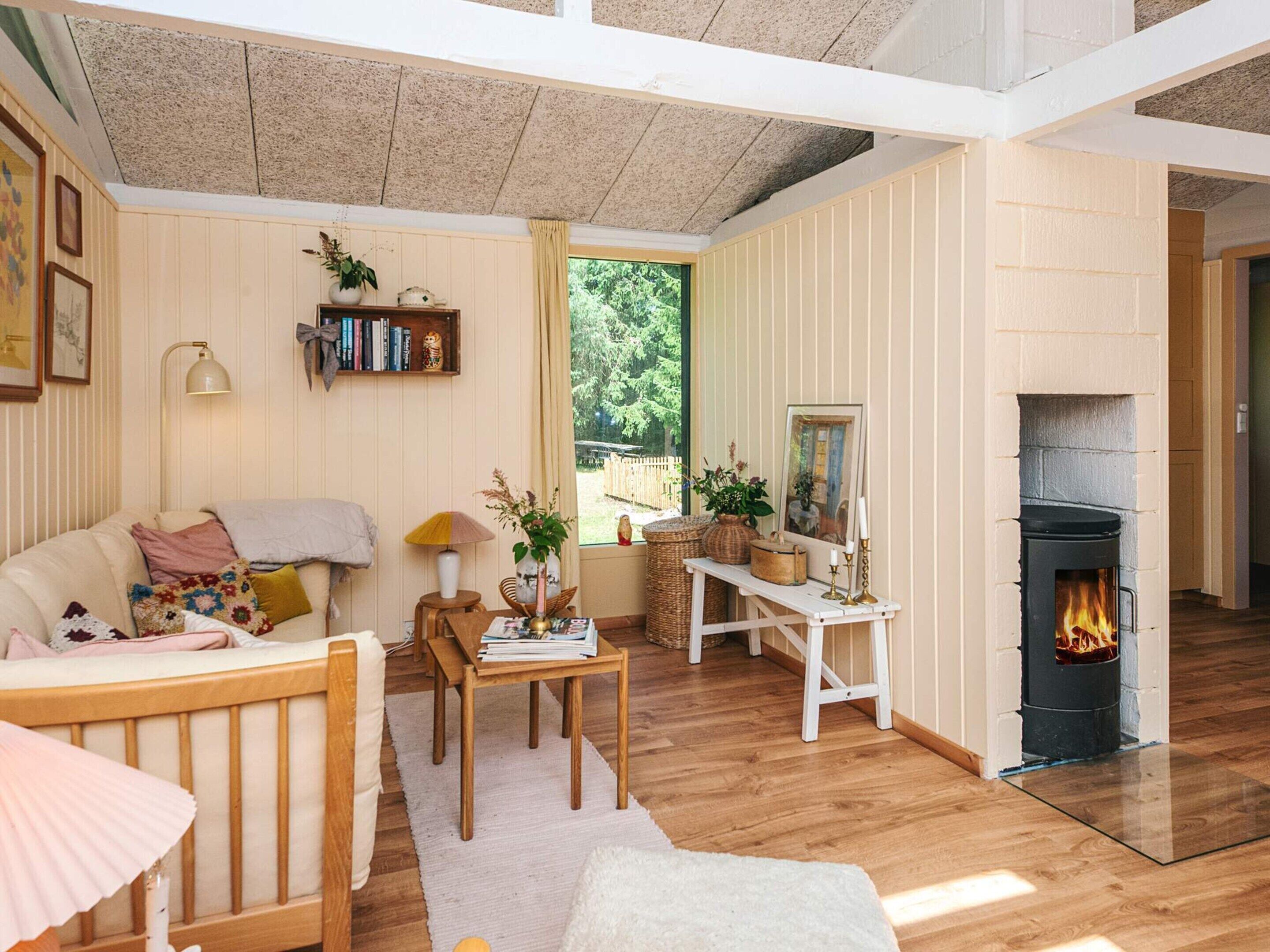 A cozy living room with a fireplace, wooden furniture, and a view of greenery outside.