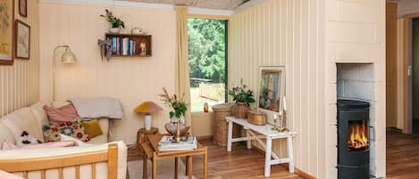 A cozy living room with a fireplace, wooden furniture, and a view of greenery outside.