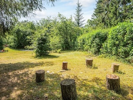 Un espacio al aire libre con césped, varios troncos de madera y abundante follaje verde.