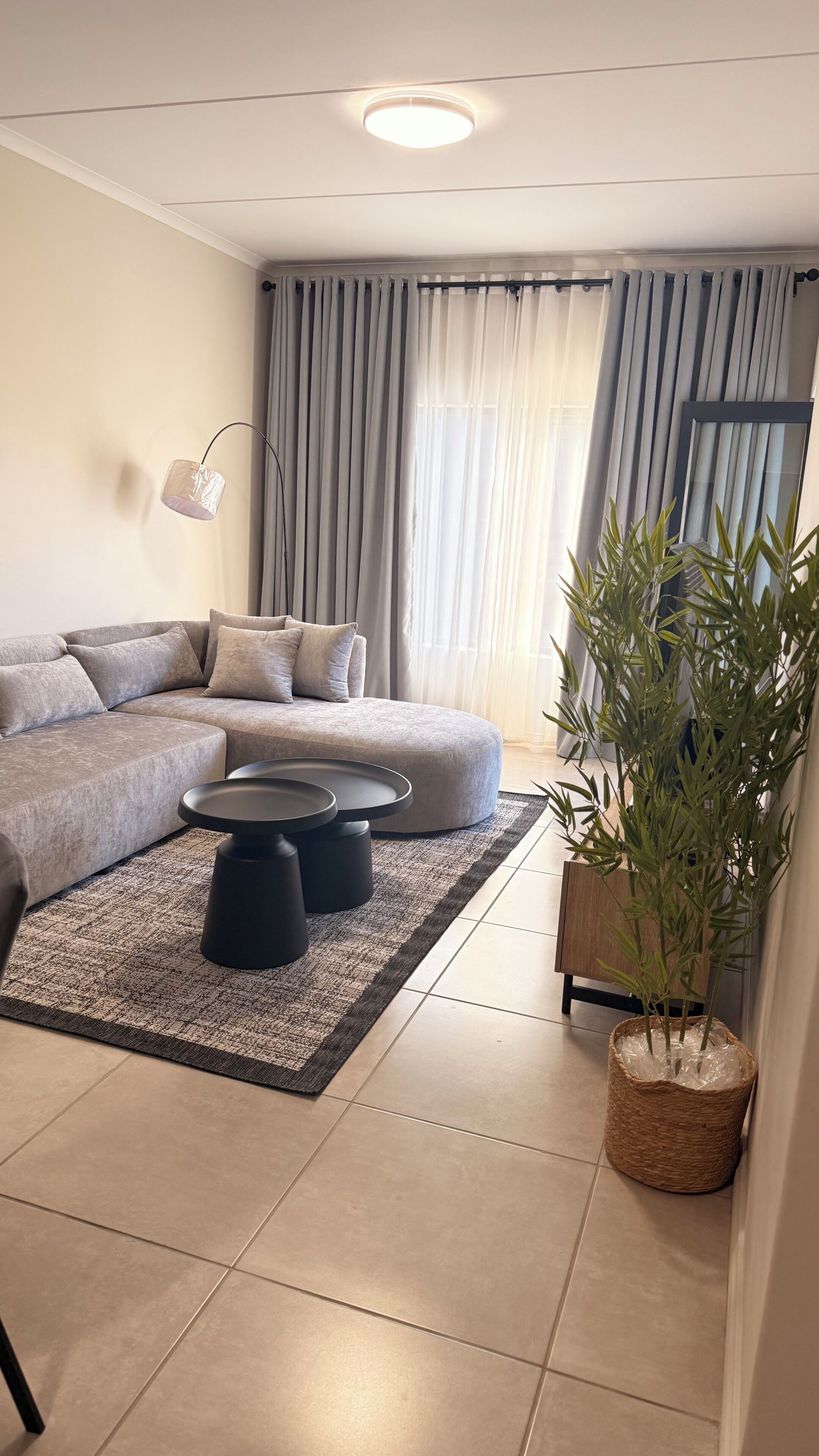 Ein modernes Wohnzimmer mit einem Ecksofa, einem runden Couchtisch, einer Stehlampe und einer Topfpflanze.