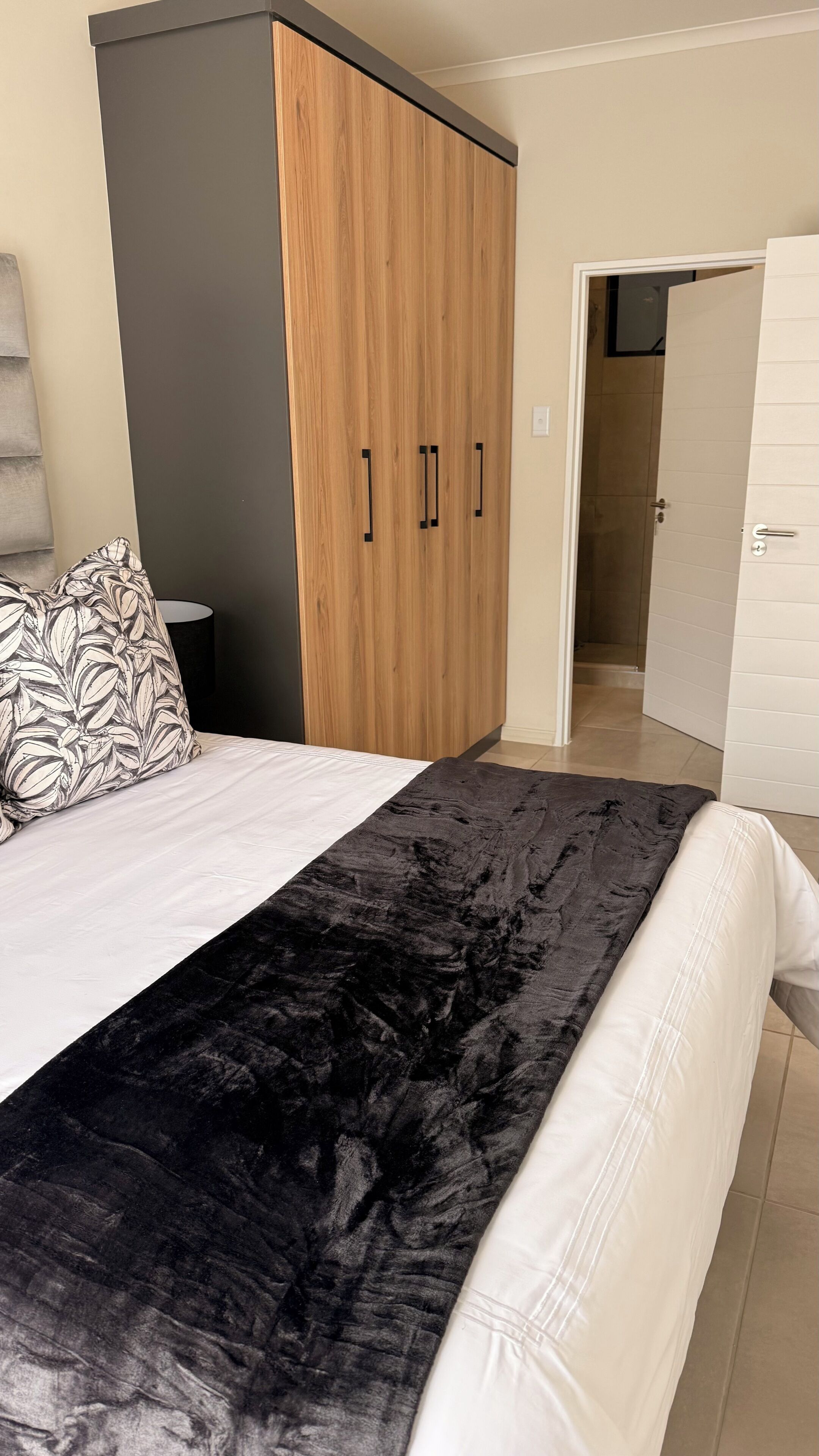 A bedroom with a bed, a wardrobe, a nightstand, and a door leading to a bathroom.