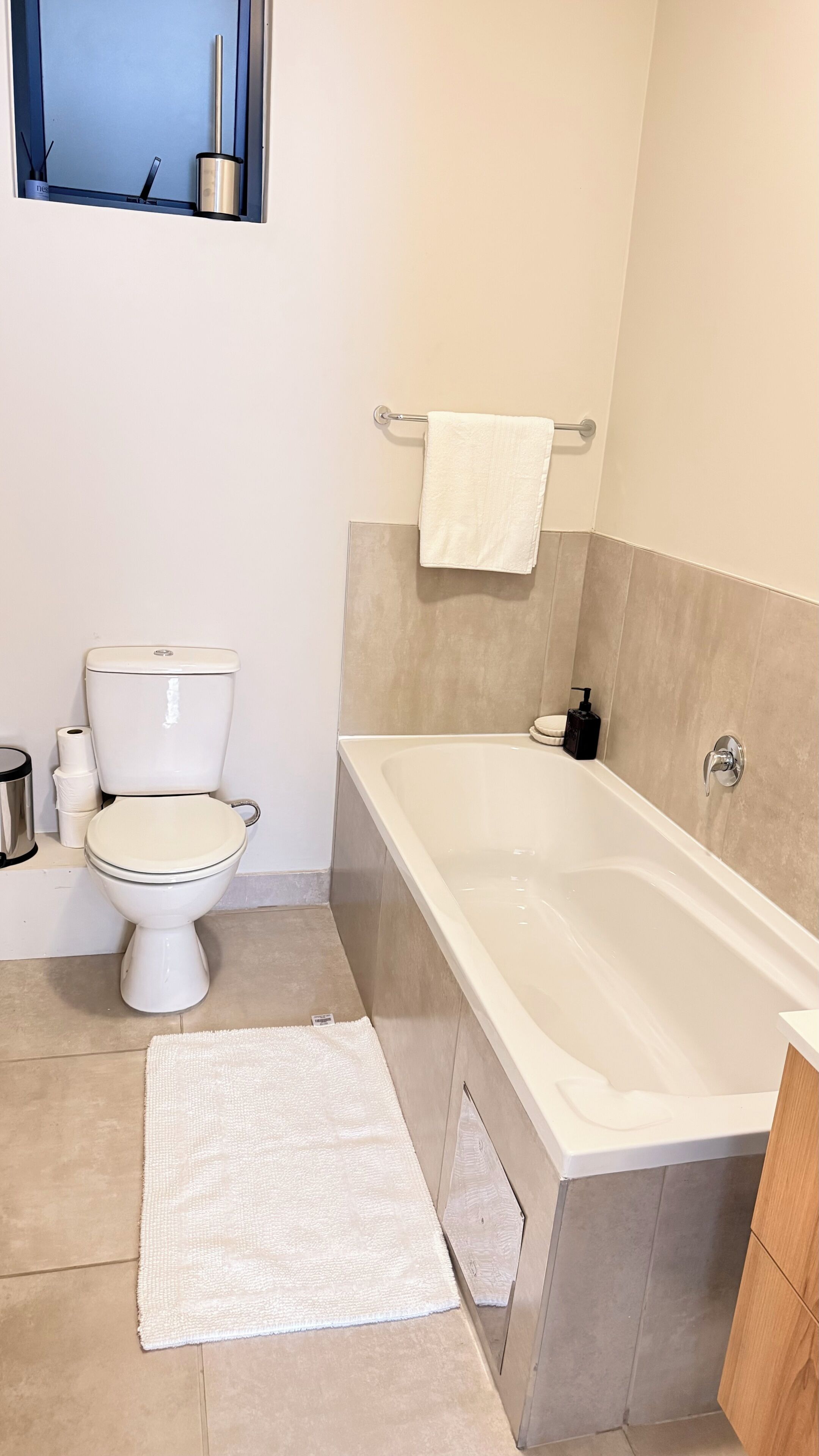 Une salle de bain avec des toilettes, une baignoire et un tapis blanc.